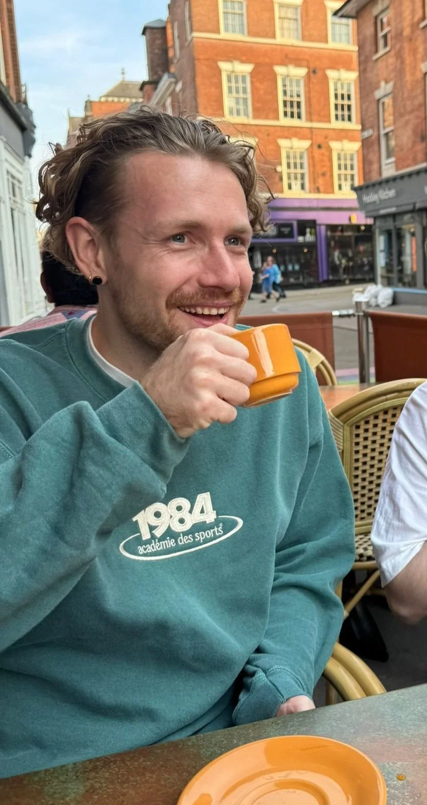 Tom smiling while holding a cup at an outdoor cafe